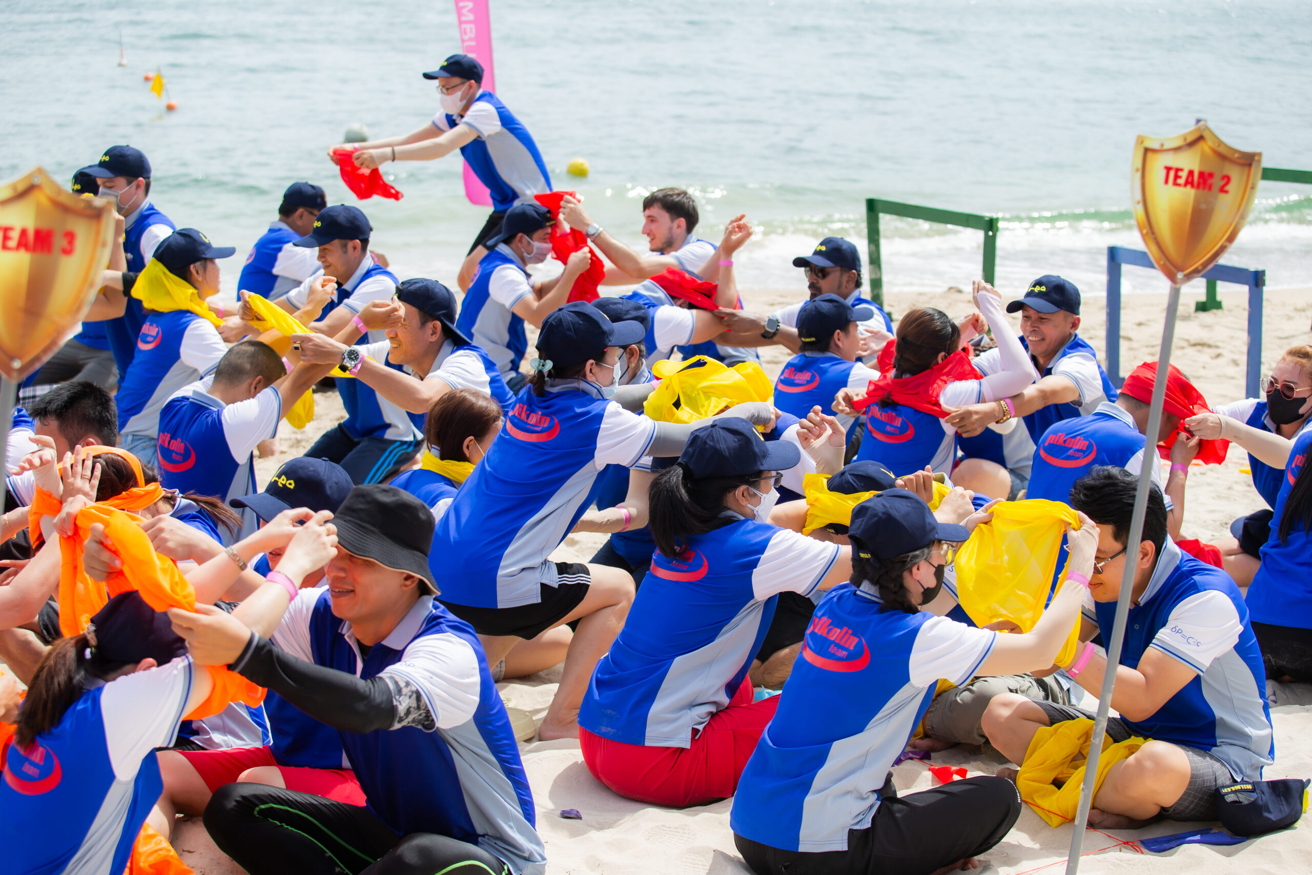 Đoàn khách mặc đồng phục xanh đỏ chơi trò team building tiếp sức trên cát.