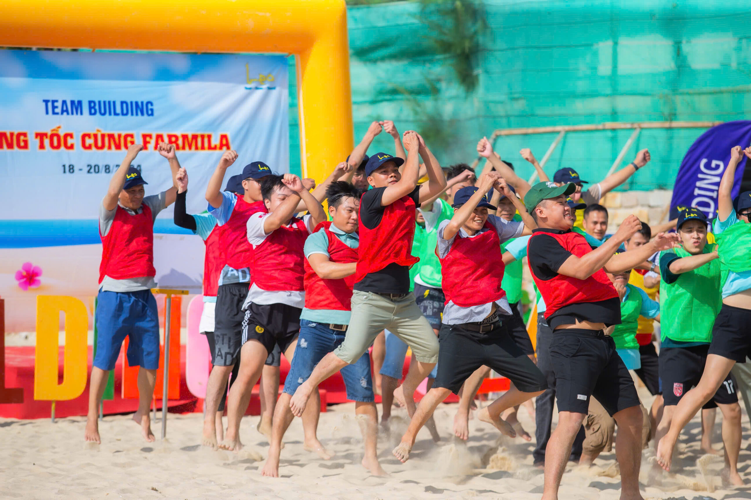 Nhóm người mặc áo đỏ vui vẻ nhảy lên cùng nhau trên cát trong sự kiện ngoài trời.