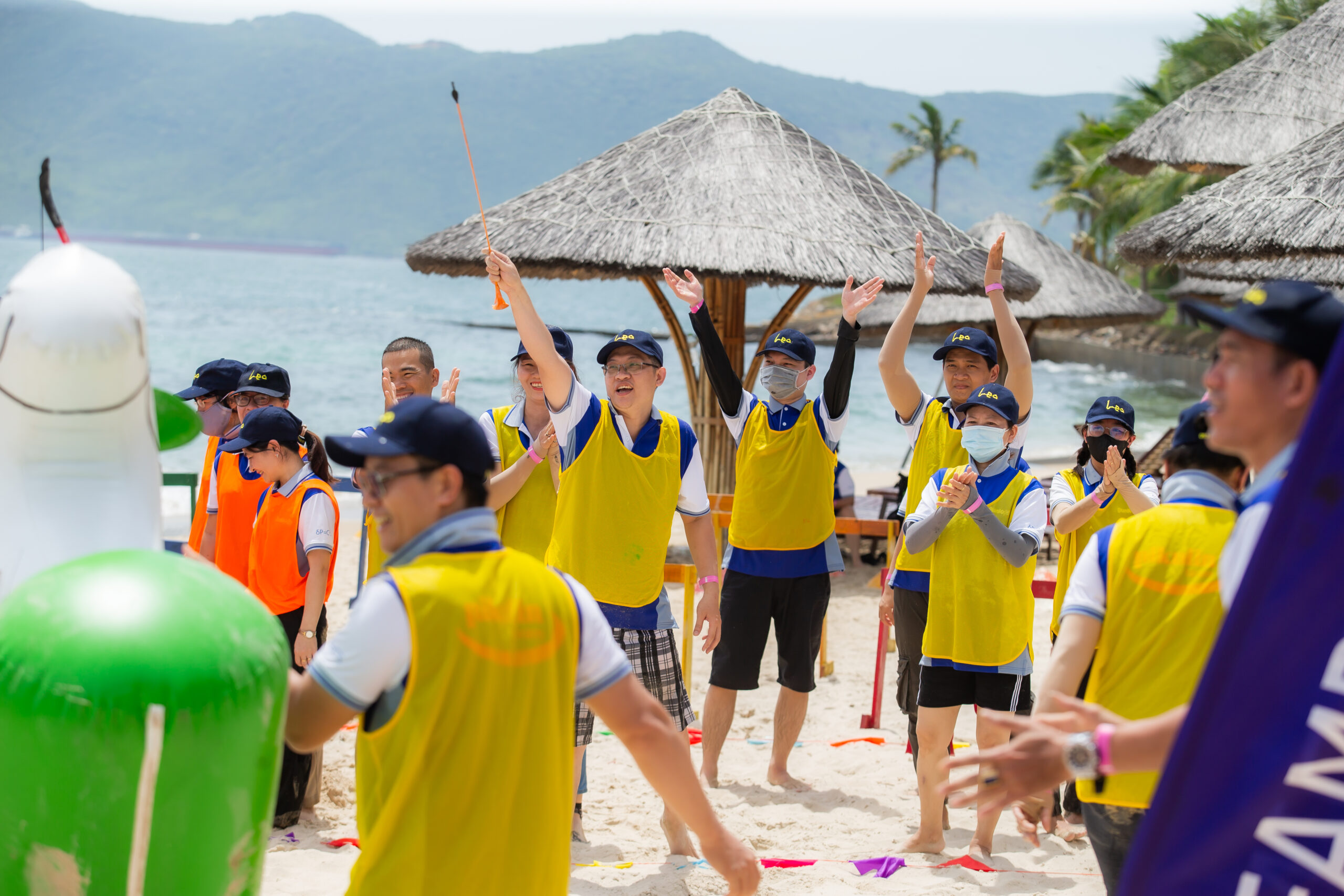Nhóm nhân viên mặc áo team màu vàng và cam cùng tham gia hoạt động team building trên bãi biển, minh họa cho hiệu quả khi chọn đơn vị tổ chức chuyên nghiệp và sáng tạo