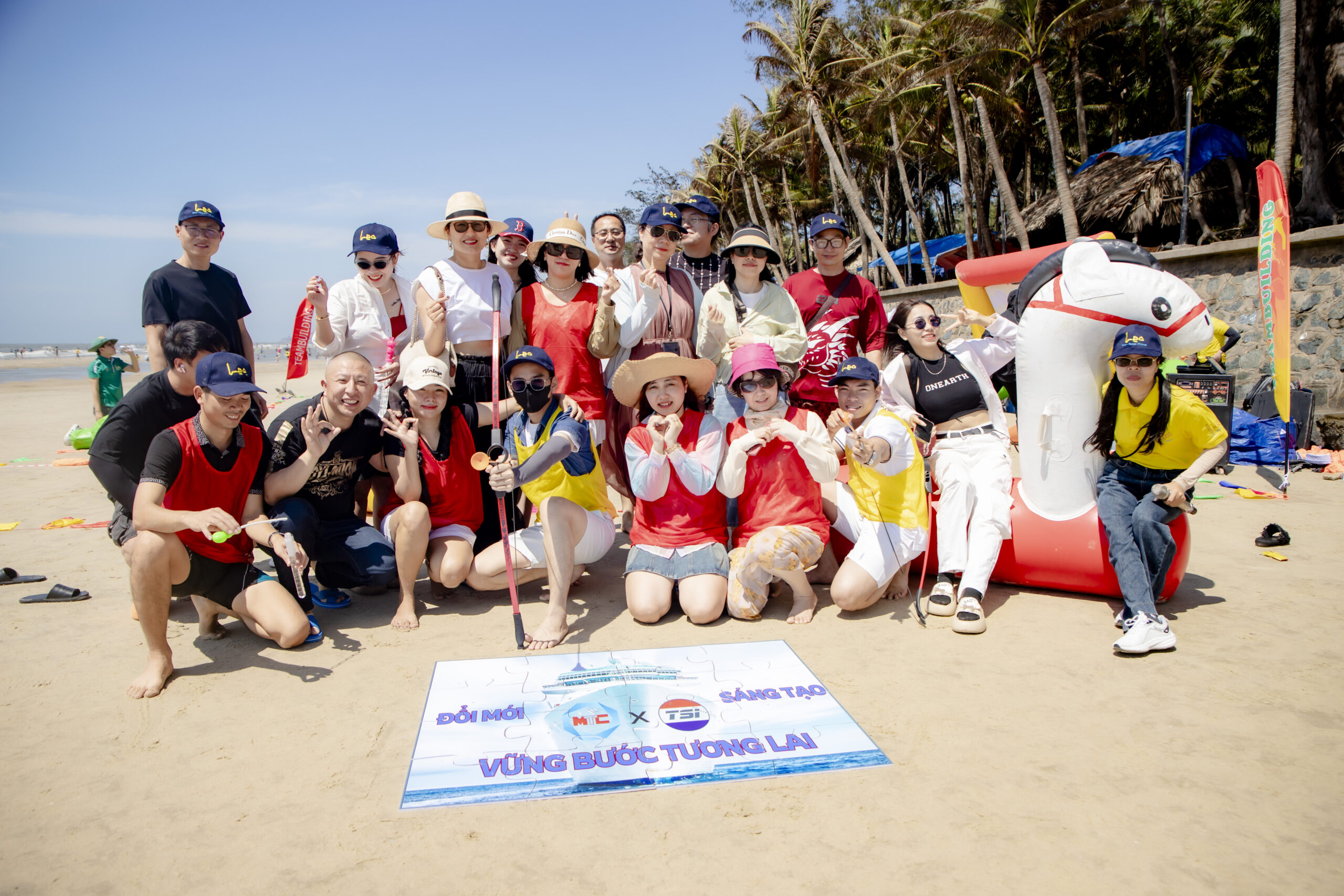 Tập thể nhân viên trong trang phục team building rực rỡ cùng chụp ảnh lưu niệm trên bãi biển, hoạt động vừa gắn kết tinh thần vừa giúp doanh nghiệp quản lý chi phí team building hiệu quả.