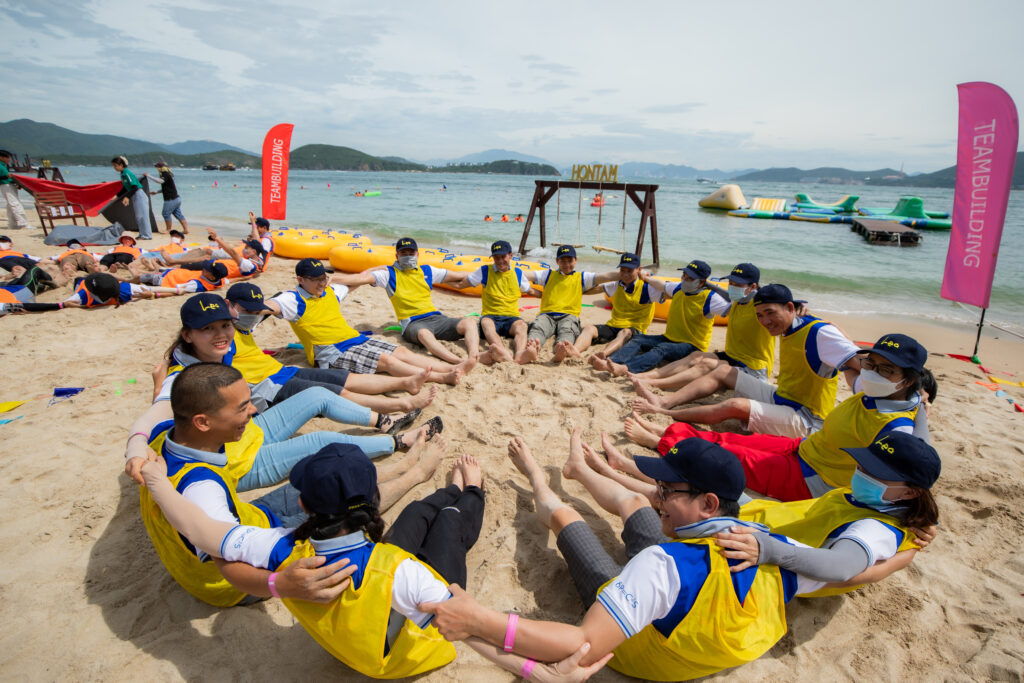 Khách mặc áo đồng phục vàng chơi team building kết nối tại bãi biển.