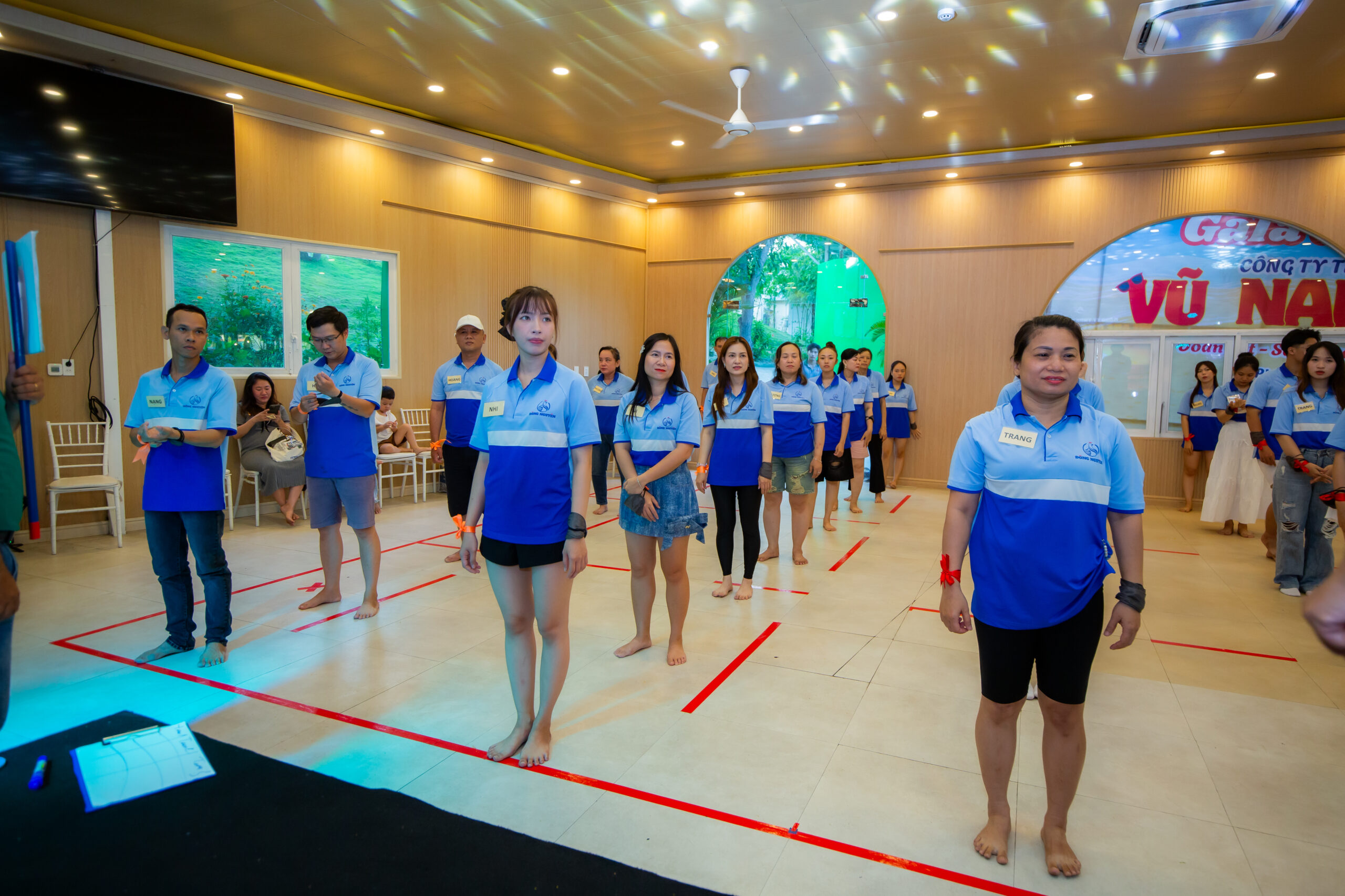 alt= “Nhân viên công ty xếp hàng tham gia hoạt động team building trong phòng, thể hiện quá trình đào tạo nội bộ hiệu quả giúp nâng cao tinh thần đồng đội và kỹ năng phối hợp.”